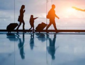 A family carries their luggage while walking through an airport, surrounded by travelers and shops.