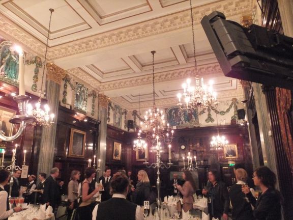 A formal dining room filled with a large group of people enjoying a meal together, surrounded by elegant decor.